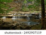 Partial view of the waterfall at roaring river falls in Tennessee standing at the rocky shoreline looking towards the wall of graffiti damage to the natural area on a sunny day in summertime