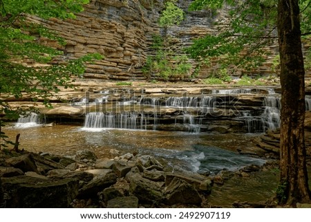 Partial view of the waterfall at roaring river falls in Tennessee standing at the rocky shoreline looking towards the wall of graffiti damage to the natural area on a sunny day in summertime