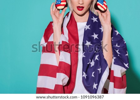 partial view of woman with american flag and cupcakes on blue backdrop, celebrating 4th july concept