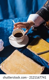 partial view of woman with cigarette near cup of coffee and vintage books on blue velour tablecloth