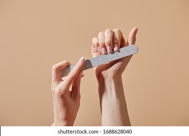 Partial view of woman filing fingernails with emery board isolated on beige