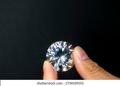 Partial view of woman holding big clear shiny diamond on black background. Jewelry business concept.