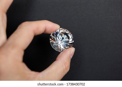 Partial view of woman holding big clear shiny diamond on black background. Jewelry business concept.