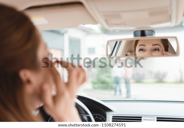 partial\
view of woman looking at mirror while driving\
car
