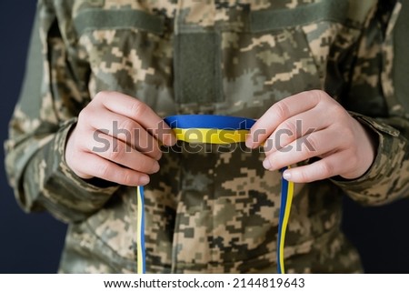partial view of woman in military uniform holding blue and yellow ribbon isolated on black
