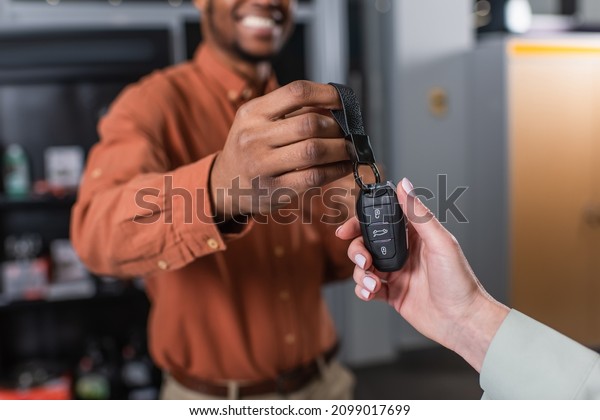 partial view of woman taking key\
from african american car dealer smiling on blurred\
background