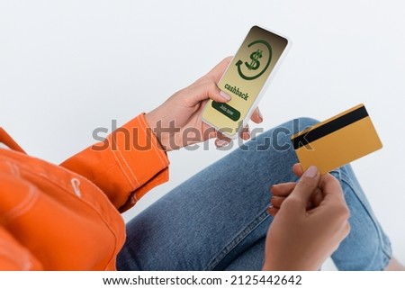 partial view of woman using smartphone with cashback on screen and holding credit card isolated on grey