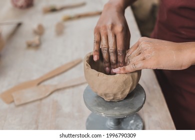 partial view of young african american woman sculpting clay pot with hands in pottery - Powered by Shutterstock