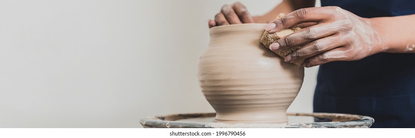 partial view of young african american woman modeling wet clay pot on wheel with sponge in pottery, banner - Powered by Shutterstock