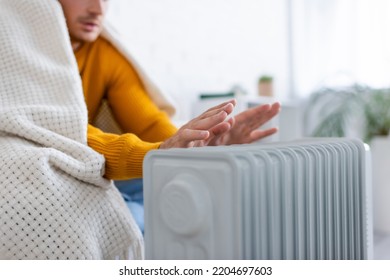 Partial View Of Young Man Covered In Blanket Sitting On Sofa And Warming Up Near Radiator Heater