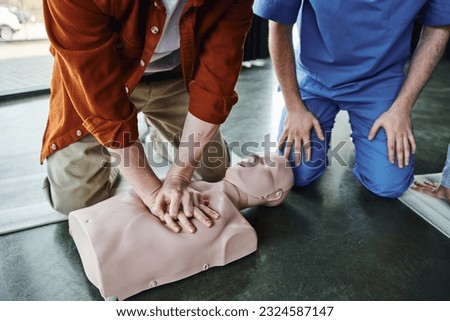 partial view of young man doing chest compressions on CPR manikin during first aid seminar near professional paramedic, cardiopulmonary resuscitation, life-saving skills and techniques concept