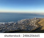 A partially cloud-covered view of Table Mountain, a flat-topped mountain in Cape Town, South Africa. Lush vegetation covers the lower slopes, and the city of Cape Town can be seen.