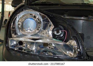 A partially disassembled headlight installed on a car in an auto repair shop with a lens and a xenon lamp - Shutterstock ID 2117085167