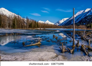 Partially Frozen Lake With Mountain Range Reflected In The Great Alaskan Wilderness.  A Beautiful Landscape Of Blue Sky, Trees, Rock, Snow, Water And Ice.  Near Seward Highway Near Anchorage, Alaska.