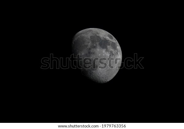 a partially lit moon in a cloudless black sky\
with visible craters on its\
surface