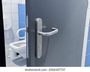 A partially open gray door with a stainless steel handle, leading into a restroom with blue and white tiled walls. - Powered by Shutterstock