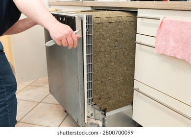 Partially pulled-out built-in dishwasher during replacement process in modern kitchen. Exposed insulation and appliance housing visible before installation. Concept of appliance replacement and home maintenance.