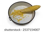 A partially shucked ear of corn in a round metal bowl. Some kernels have been cut off and are scattered in the bowl.