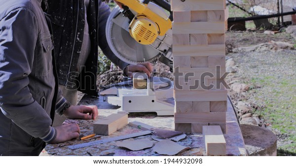 partially visible father and son working\
at a circulating woodworking machine sawing lumber into small\
blocks, family training in craft and trimming\
skills