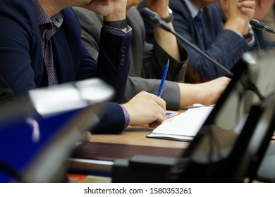 Participants In A Business Meeting With Notebooks, Pens, Watches, And Monitors Carefully Listen To The Speaker. Work Time. Business Style. Close-up. Shallow Depth Of Field.