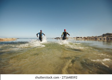 Participants running into the water for start of a triathlon. Two triathletes rushing into water for swim portion of race.