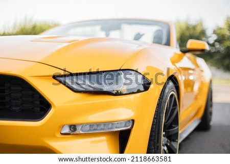 Particle view of yellow brand new modern luxury sport car parked outdoors. Headlights and hood of sport yellow car. Car detail