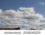 A partly cloudy sky with birds on a rooftop, A clear blue sky with white fluffy clouds, A partly cloudy sky. Light gray and white clouds