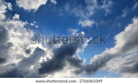 A partly cloudy sky, featuring white cumulus clouds alongside darker, denser clouds against a blue backdrop, displays a mix of white, fluffy clouds and darker, potentially rain-bearing clouds, typical of changing weather condition