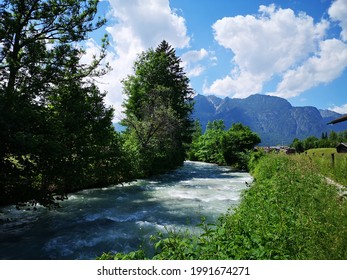 The Partnachklamm in a landscape a river that goes through a beautiful landscape.  Surrounded by trees and green grass.  In the background you can see the mountains.