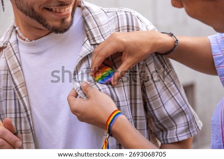 Partner lovingly attaching a pride rainbow badge to a man's shirt, showing support, love, and lgbtq plus pride