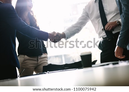 Partners concluding deal and shaking hands in the presence of team members. Businessmen shaking hands in board room and finishing up a meeting.