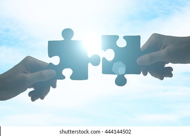 Partnership concept with hands putting puzzle pieces together on sky background with sunlight