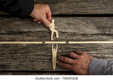 Partnership concept using paper cut outs of men with one holding up a bridge in a gap so that the other can walk across over rustic wooden background.