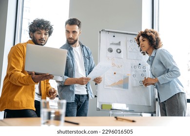 Partnership, teamwork. Multiracial business people are working together on a project, brainstorming, stand near whiteboard with financial charts, predicting income, analyzing risks, setting goals