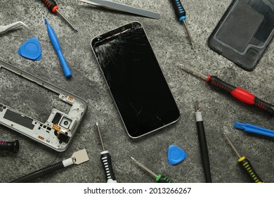 Parts of damaged smartphone and repair tool set on grey table, flat lay
