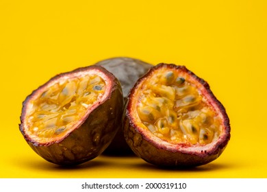 Parts of Maracuja or Brazilian tropical passion fruit showing pulp flesh with black seeds. Studio food still life against a yellow background