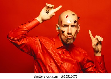 Party Boy Concept. Handsome Young Bald 40 Years Old Man With Confetti Stars On His Face Dancing And Looking Happy, Funny Over Scarlet Background. Copy-space. Studio Shot