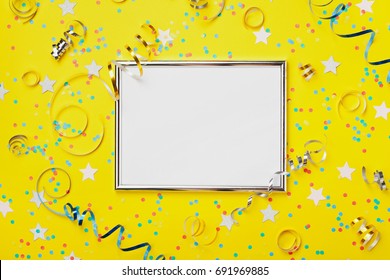 Party, Carnival Or Birthday Background Decorated Silver Frame With Colorful Confetti And Streamer On Yellow Table Top View. Flat Lay Style. Holiday Mockup. Greeting Card With Copy Space.