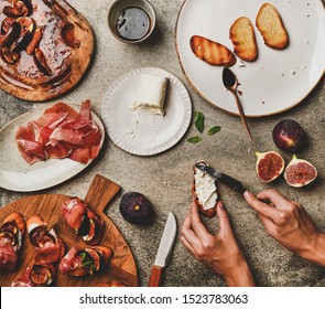 Party Or Catering Food Cooking. Flat-lay Of Crostini With Prosciutto, Grilled Figs And Female Hands Spreading Goat Cheese On Bread Over Grey Concrete Table Background, Top View