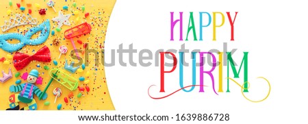 Party colorful noisemaker, mask and cute clown doll over yellow wooden background. Top view, flat lay