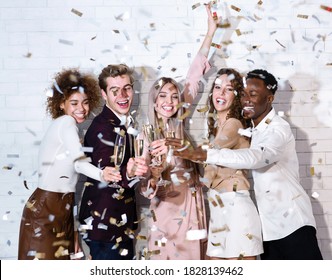 Party Concept. Diverse Guys And Girls Clinking Glasses Under Falling Confetti Celebrating Holiday Indoor.