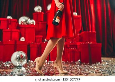 Party concept. Sexy legs of woman in glamour style shoes with silver luxury confetti on the floor. New Year and Christmas holidays. Against the background of red gift boxes and disco balls.