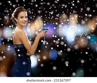 Party, Drinks, Holidays, Christmas And People Concept - Smiling Woman In Evening Dress Holding Cocktail Over Night Lights And Snow Background