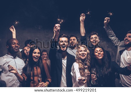 Party with friends. Group of cheerful young people carrying sparklers and champagne flutes