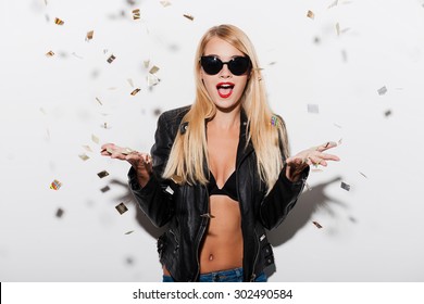 Party girl. Surprised young woman in black bra and leather jacket stretching out her hands while confetti falling on her