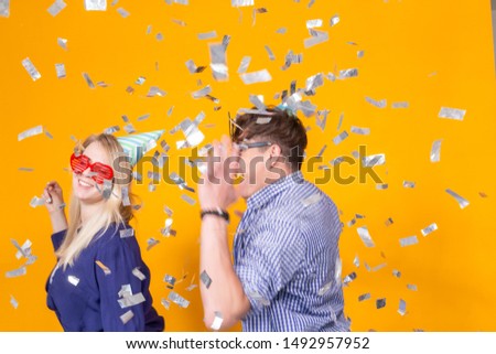 Party, holiday and birthday concept - Young funny couple dancing while standing against yellow background with confetti