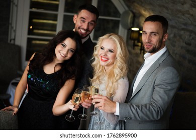 Party, holiday with friends concept. Four people with champagne glasses celebrating and toasting in restaurant. Two men and two women in elegant evening clothes, suits and dresses night out indoors.