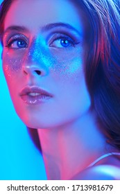 Party and holiday style. Beautiful girl with shiny glitter freckles posing in blue and pink light. Cosmetics and makeup.
