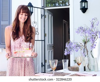 Party Hostess Carries A Tray Of Drinks To The Table In A Domestic Garden Environment 