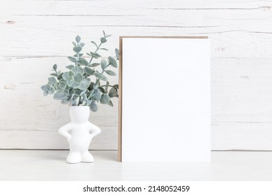 Party Invitation Mockup On A Light Background With Flowers. Vertical White Card 5x7 On The Table Against A Light Wall.